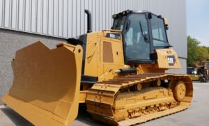 Trator de esteira Caterpillar D6K XL amarelo com lâmina frontal e cabine envidraçada em área industrial