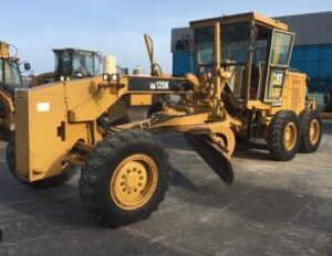 Motoniveladora Caterpillar 120K amarela estacionada em pátio industrial