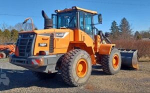 Carregadeira de rodas Doosan com caçamba frontal, cabine fechada e pneus largos em terreno de cascalho