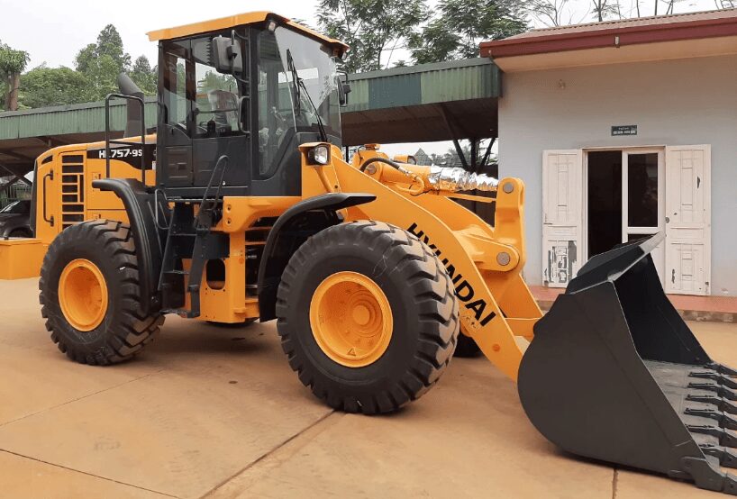 Pá carregadeira Hyundai HL757-9S amarela com caçamba frontal em área externa