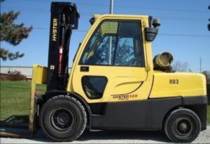 Empilhadeira Hyster amarela com cabine fechada, mastro preto e garfos em ambiente externo