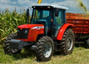Trator agrícola Massey Ferguson vermelho com cabine fechada e reboque em área rural